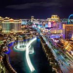 Night view of the Las Vegas Strip featuring the Bellagio Fountains, Paris Las Vegas Eiffel Tower, and illuminated casino resorts.