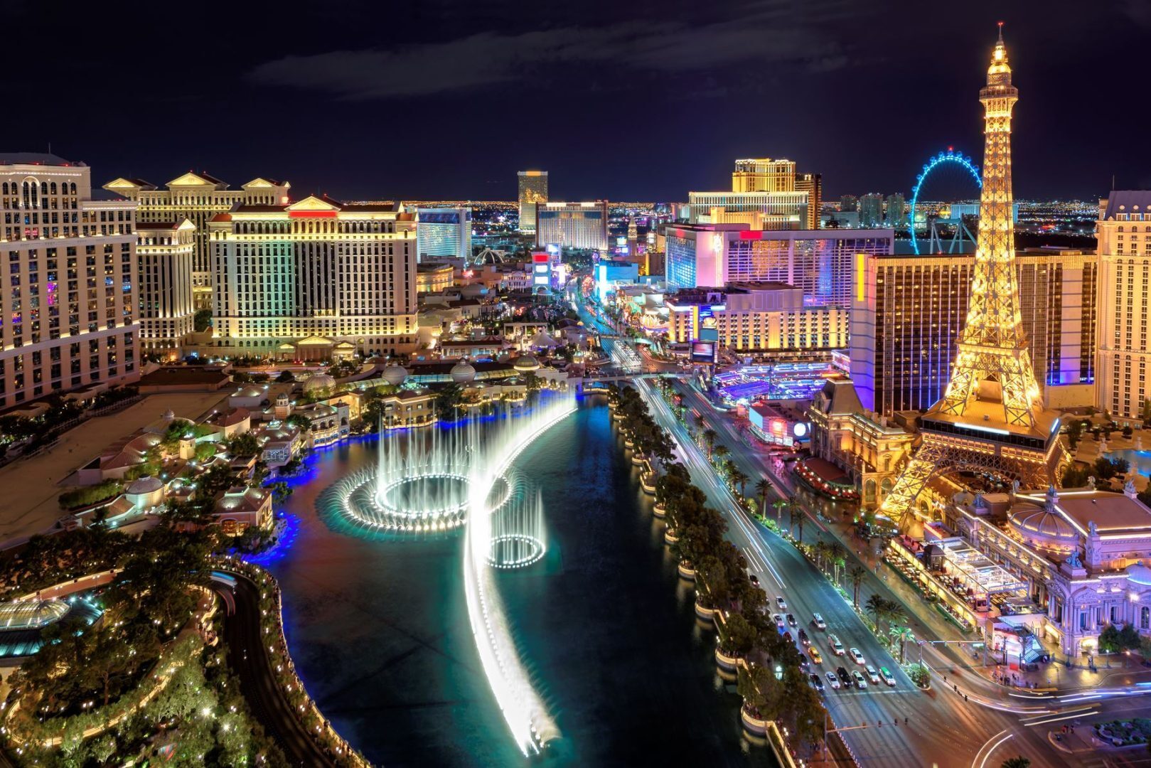 Night view of the Las Vegas Strip featuring the Bellagio Fountains, Paris Las Vegas Eiffel Tower, and illuminated casino resorts.