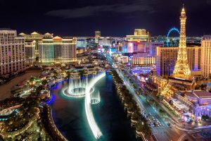 Night view of the Las Vegas Strip featuring the Bellagio Fountains, Paris Las Vegas Eiffel Tower, and illuminated casino resorts.