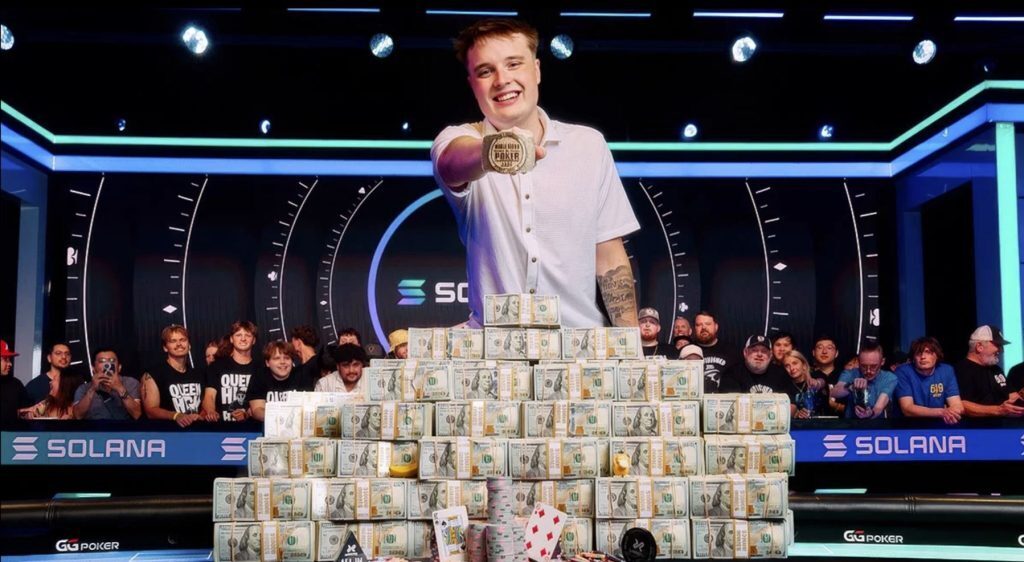 Lucas Jumalon celebrates after winning the 2026 WSOP Main Event, posing behind stacks of prize money while holding the championship bracelet.