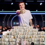Lucas Jumalon celebrates after winning the 2026 WSOP Main Event, posing behind stacks of prize money while holding the championship bracelet.